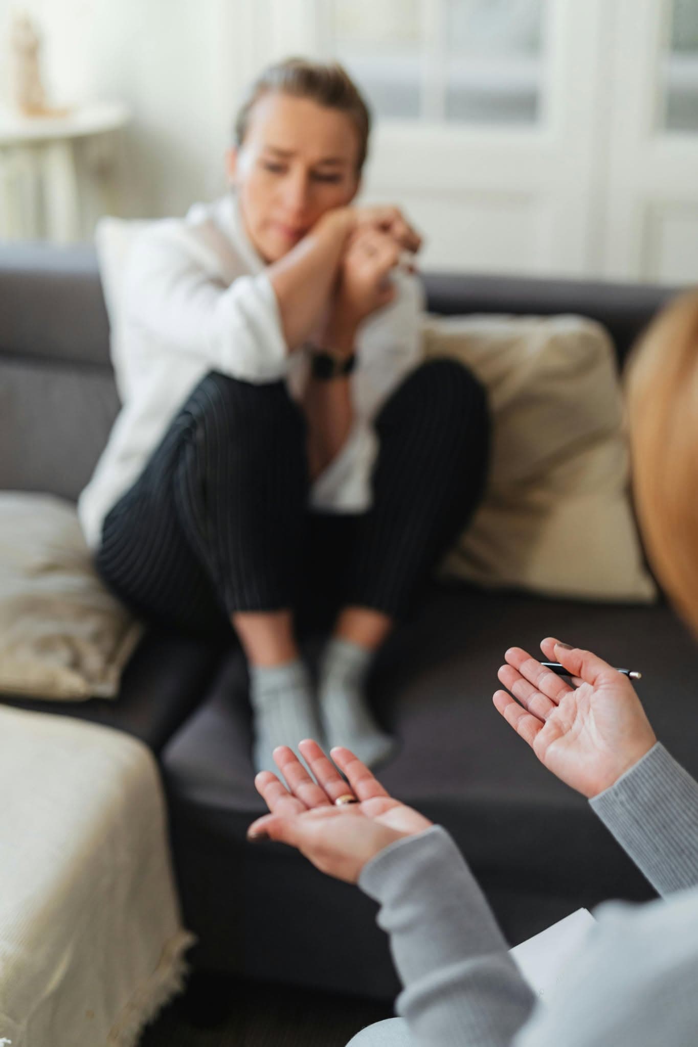 Thérapeute gesticulant avec ses mains devant une femme pensive assise sur un canapé gris.