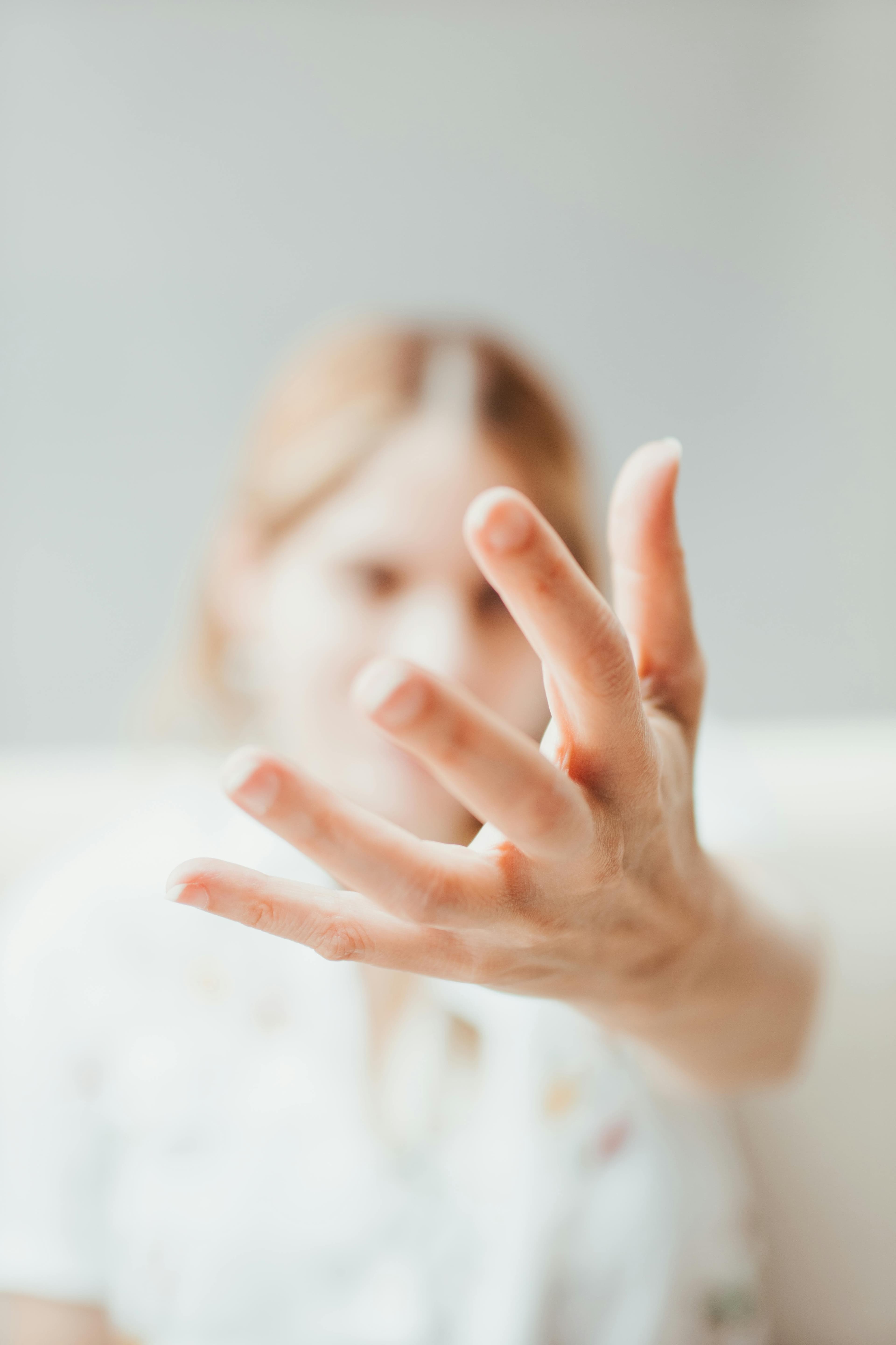 Gros plan d'une main tendue vers l'avant, avec une femme floue en arrière-plan.